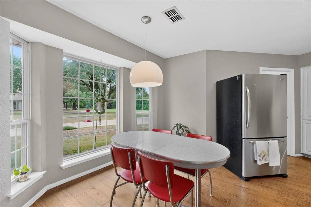 1151 Lynn Way, Waxahachie, TX 75165 Bay window with multiple panes, wood-finish flooring, a contemporary pendant light fixture, a stainless steel refrigerator, and light grey wall paint