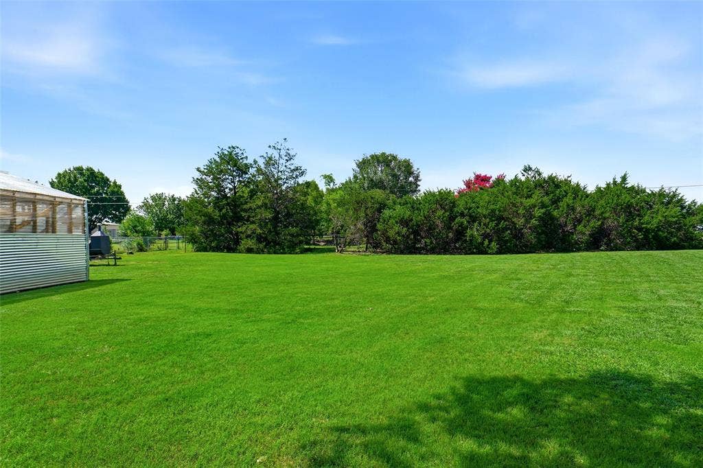 Expansive green lawn with mature perimeter landscaping and a corrugated metal green house