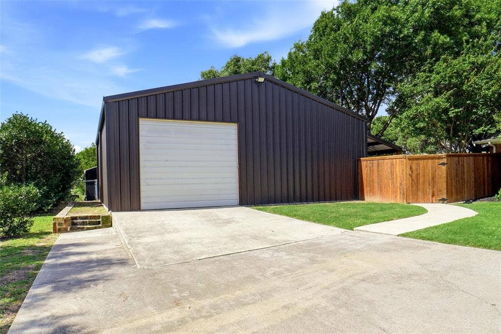 Barndominium with a white garage door, concrete driveway, and a curved concrete walkway