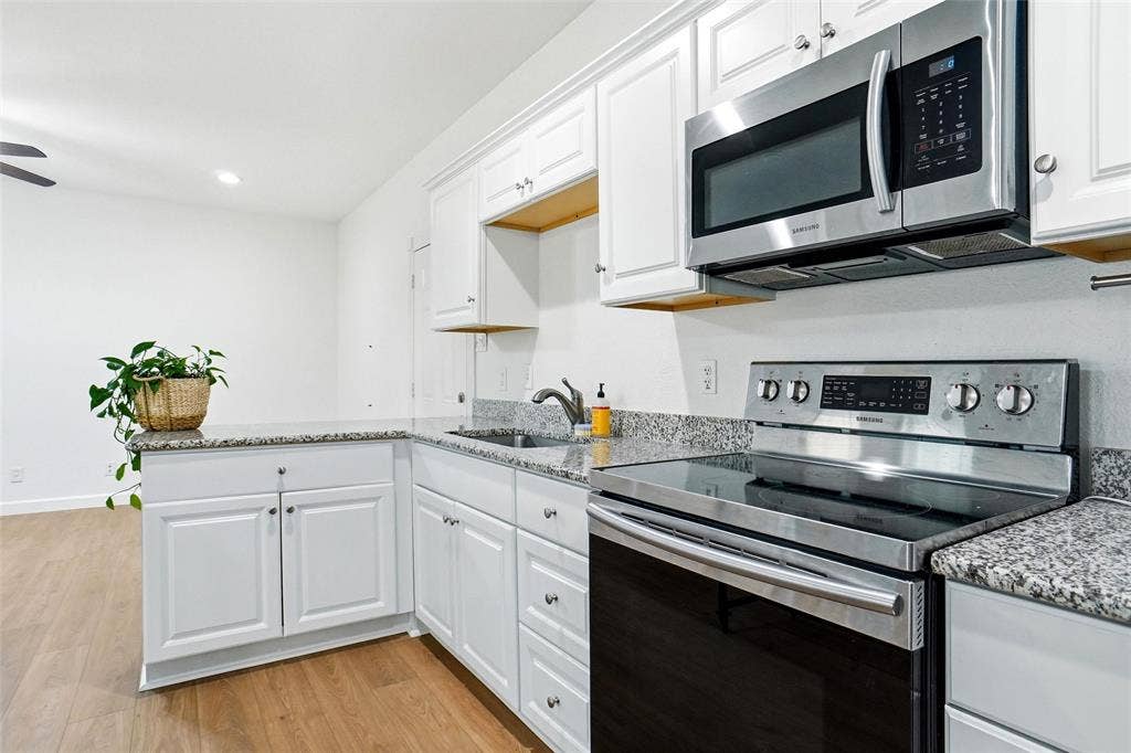 Kitchen featuring white cabinetry, granite countertops, stainless steel appliances including a range and over-the-range microwave, and LVP wood-finish flooring