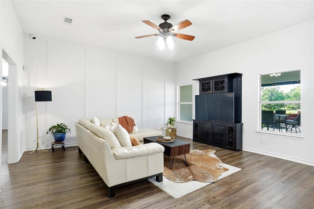 Spacious living area featuring LVP wood-style flooring, white panel accent walls, and a ceiling fan with integrated lighting.