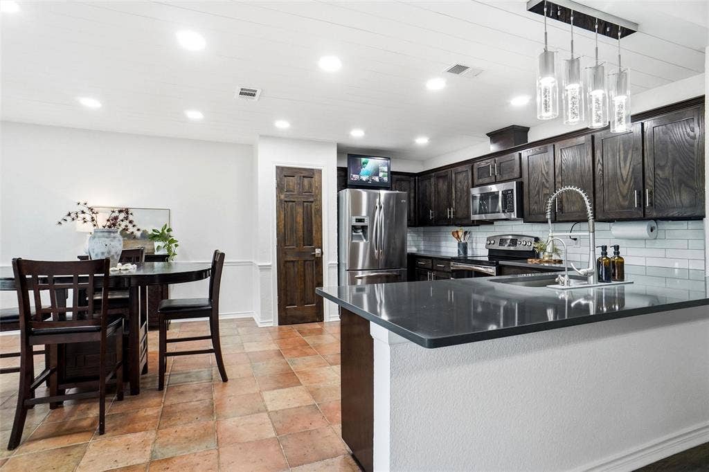 Kitchen featuring dark wood cabinetry, stainless steel appliances, quartz countertop, and a subway tile backsplash