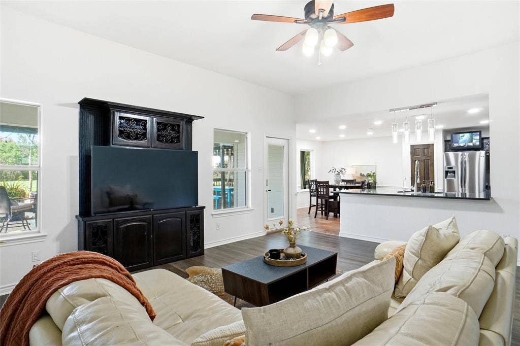 Open-concept living area featuring LVP wood-style flooring, a ceiling fan, and multiple windows for natural light.