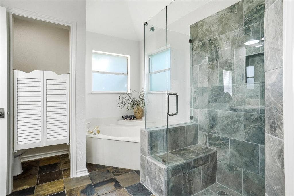 Glass-enclosed shower with slate-style tile, built-in bench, and corner soaking tub