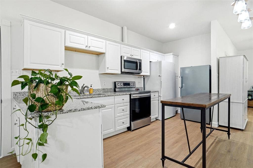 Kitchen featuring white cabinetry, stainless steel appliances, light granite countertops, and LVP wood-finish flooring