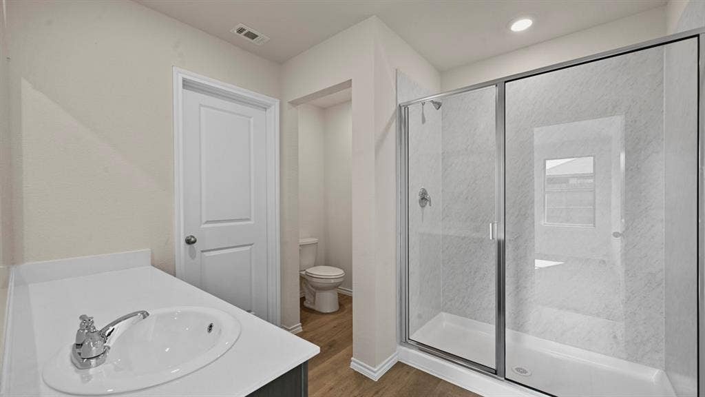 1663 Blaire Drive, Tyler, TX 75702 Bathroom featuring a clear glass shower enclosure with chrome fixtures, a single vanity with an undermount sink, and wood-finish flooring