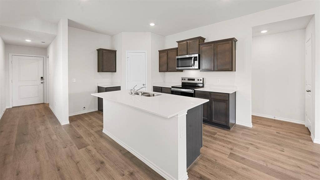 1663 Blaire Drive, Tyler, TX 75702 Kitchen featuring a central island with an integrated double sink, wood-finish flooring, white countertops, dark wood-finish cabinetry, and stainless steel appliances including a microwave and range