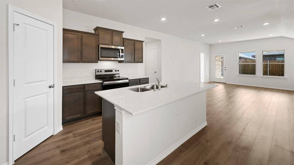 1663 Blaire Drive, Tyler, TX 75702 Kitchen featuring a central island with an undermount sink, dark wood cabinetry, white countertops, stainless steel appliances, and wood-finish flooring