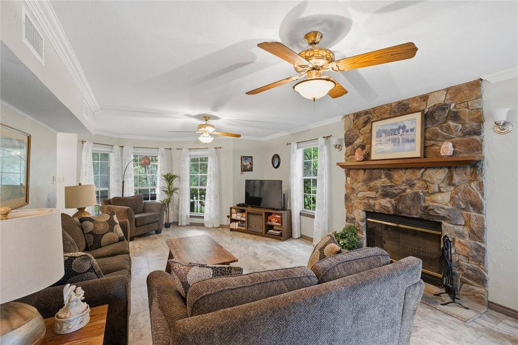 2746 Hopson Drive, Athens, TX 75752 Spacious living area featuring a stone-clad fireplace with a wood mantel, multiple windows, tile flooring, and crown molding