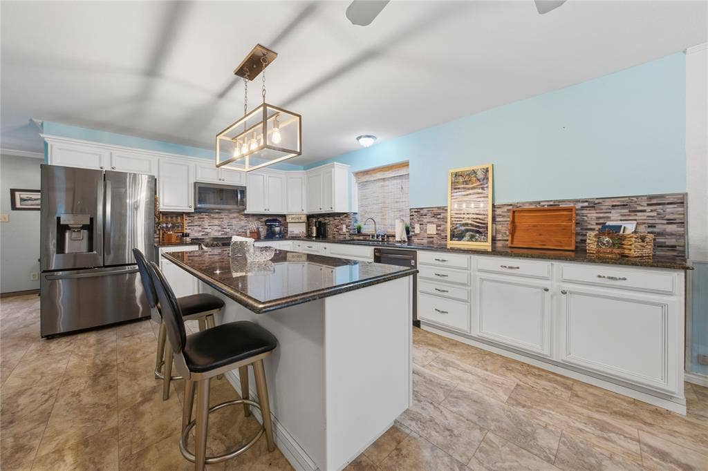 2746 Hopson Drive, Athens, TX 75752 Kitchen featuring an island with seating, dark countertops, white cabinetry, stainless steel appliances, and a mosaic tile backsplash
