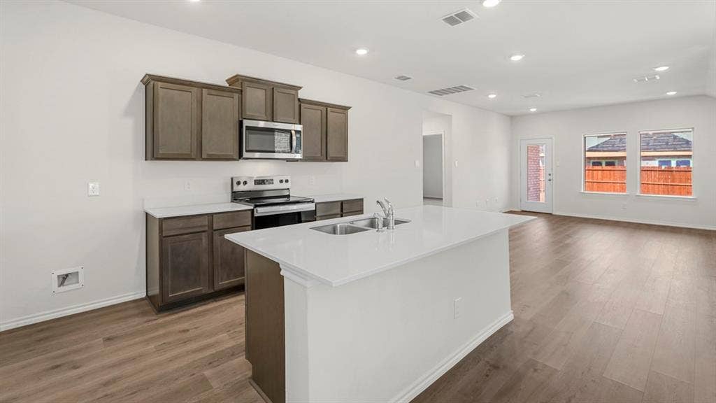 1659 Blaire Drive, Tyler, TX 75702 Open concept kitchen featuring an island with an integrated sink, white countertops, dark wood-finish cabinetry, stainless steel appliances, and recessed lighting