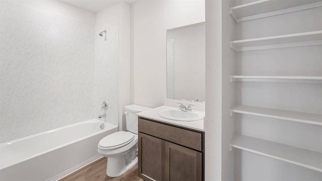1659 Blaire Drive, Tyler, TX 75702 Bathroom featuring a built-in tub with shower, single vanity with a solid surface countertop, wood-finish flooring, and integrated open shelving