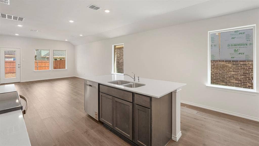 1659 Blaire Drive, Tyler, TX 75702 Kitchen island featuring a dual-basin stainless steel sink, integrated dishwasher, and light-toned solid surface countertop