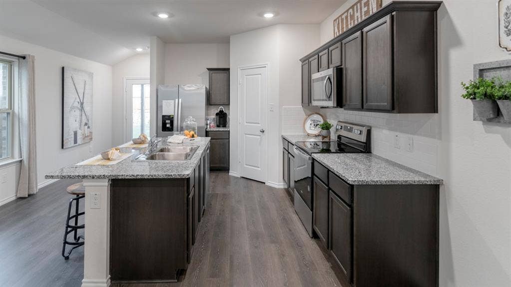 1627 Blaire Drive, Tyler, TX 75702 Open-concept kitchen featuring an expansive center island with dual sinks, light-toned stone-finish countertops, dark wood-finish cabinetry, stainless steel appliances, and wood-finish flooring