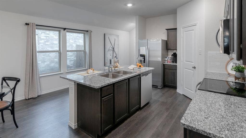 1627 Blaire Drive, Tyler, TX 75702 Kitchen featuring a central island with dual sinks, granite countertops, wood-finish flooring, dark cabinetry, and integrated stainless steel appliances