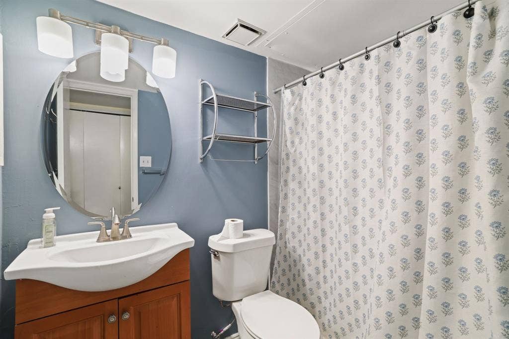 1037 Whitewater Trail, DeSoto, TX 75115 Bathroom featuring a wood-finish vanity with an integrated white sink, a circular mirror, and a three-light vanity fixture