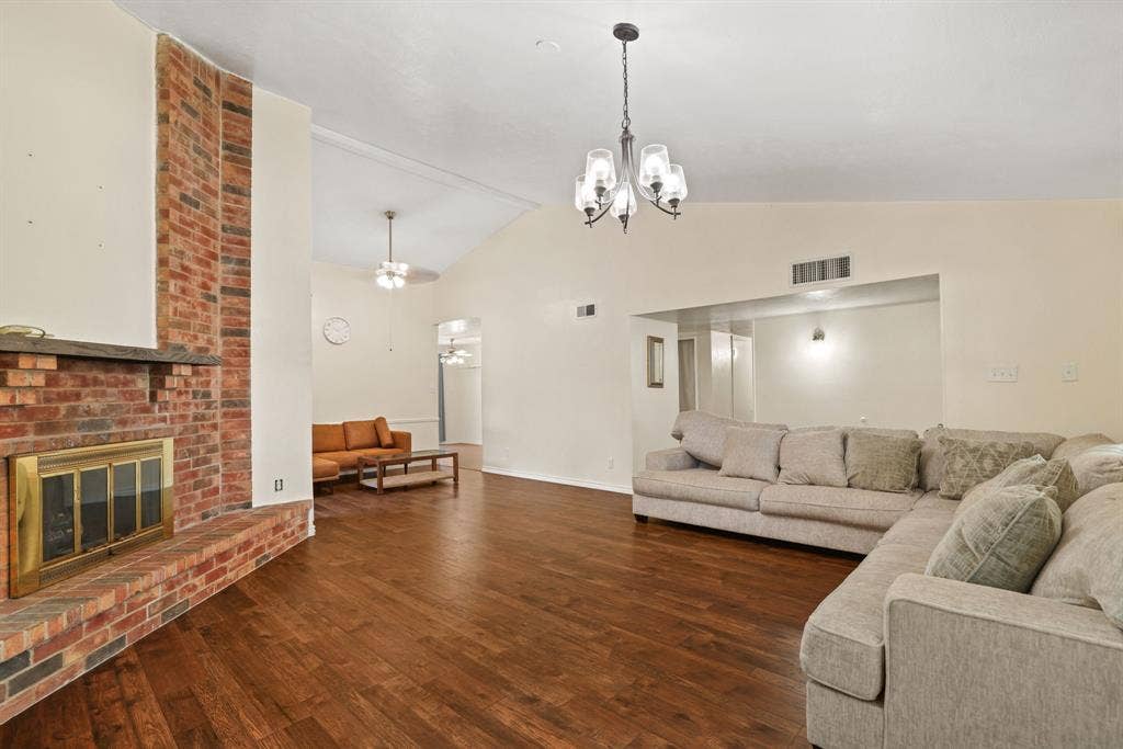 1037 Whitewater Trail, DeSoto, TX 75115 Spacious living area featuring a prominent brick fireplace with a brass firebox, wood-finish flooring, and a vaulted ceiling with a ceiling fan
