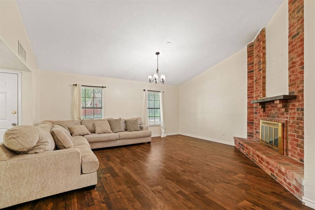 1037 Whitewater Trail, DeSoto, TX 75115 Spacious living area featuring a prominent brick fireplace with a dark wood mantel, high vaulted ceilings, and rich wood-finish flooring