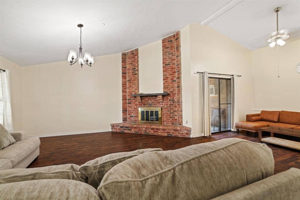 1037 Whitewater Trail, DeSoto, TX 75115 Spacious living area featuring a prominent brick fireplace with a dark mantel, wood-finish flooring, and a vaulted ceiling