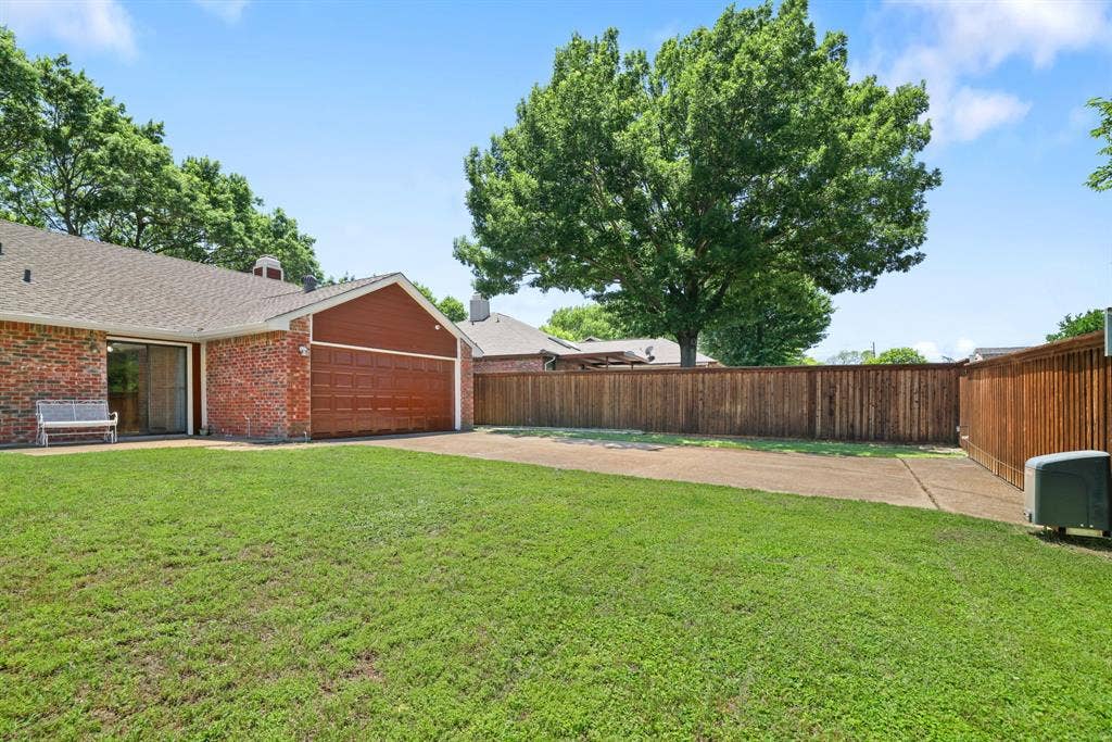 1037 Whitewater Trail, DeSoto, TX 75115 Brick exterior featuring an attached two-car garage with a paneled door, a sliding glass door, a large grassy area, and a wood privacy fence