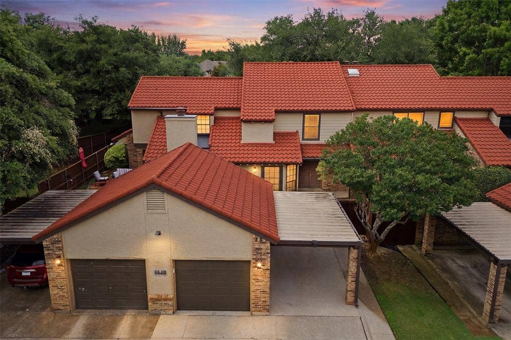 4130 Proton Drive, #47B, Addison, TX 75001 Stunning twilight aerial view of 4130 Proton Dr. #47B, showcasing the signature clay tile roof, one-car garage, and covered parking for an additional vehicle.