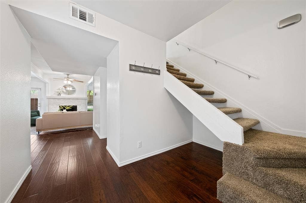 4130 Proton Drive, #47B, Addison, TX 75001 Welcoming entry with hardwood floors, a coat hook landing station, and carpeted staircase leading to the upper level — with a direct view into the living room and fireplace beyond.