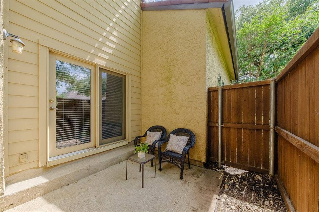 4130 Proton Drive, #47B, Addison, TX 75001 Private fenced back patio with a sliding glass door, wicker seating, and mature tree canopy overhead — a quiet outdoor space tucked away from the street.