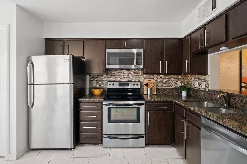 4130 Proton Drive, #47B, Addison, TX 75001 Generous kitchen storage with full-height espresso cabinets, stainless steel appliance suite, granite countertops, and a mosaic tile backsplash running the full width of the cooking wall.
