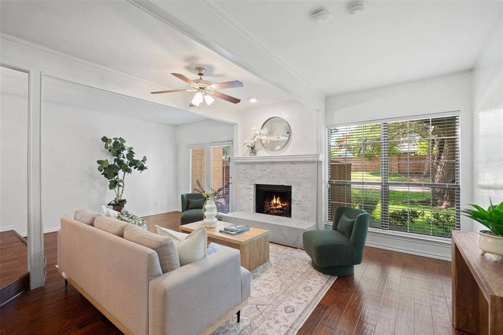 4130 Proton Drive, #47B, Addison, TX 75001 Bright and open living area with hardwood floors, beamed ceiling detail, ceiling fan, and a wall of windows overlooking the lush greenery outside — a rare find in a condo setting.