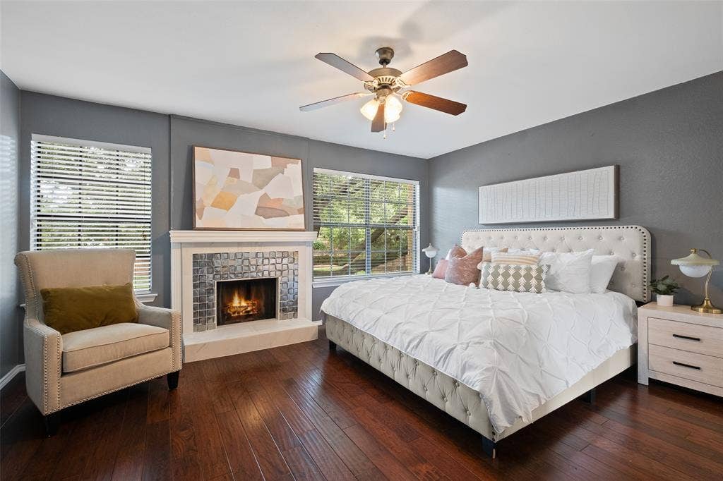 4130 Proton Drive, #47B, Addison, TX 75001 Primary bedroom showcasing the fireplace, large windows with tree views, hardwood floors, and ample space for a king-size suite — a true retreat within the home.