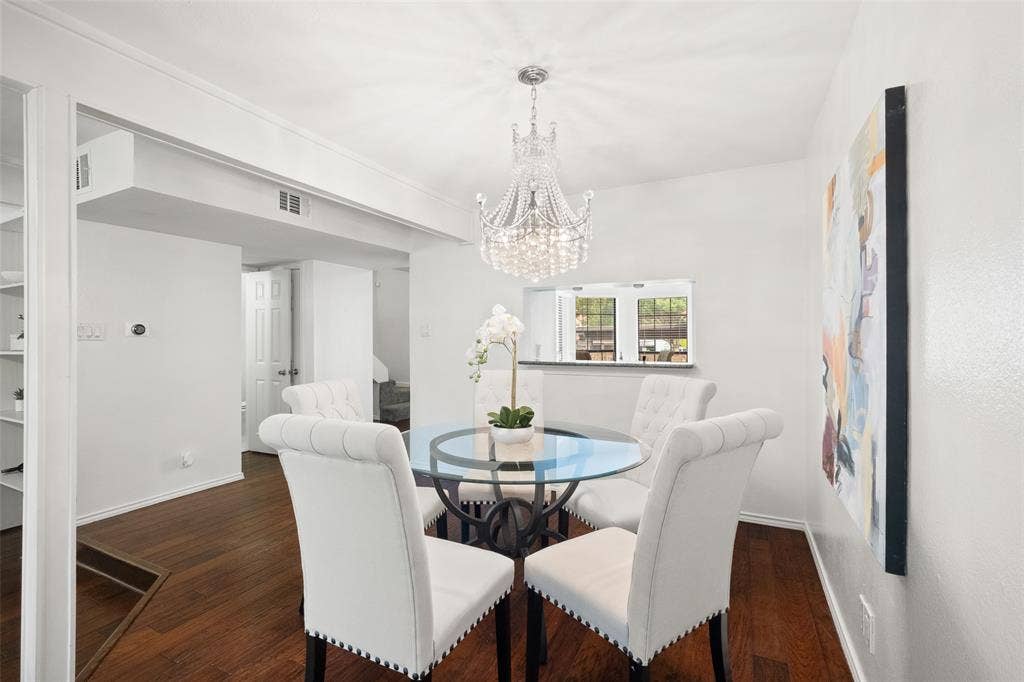 4130 Proton Drive, #47B, Addison, TX 75001 Elegant dining room with a statement crystal chandelier, glass-top table, hardwood floors, and open sight lines into the living area — a natural gathering space for dinner parties.