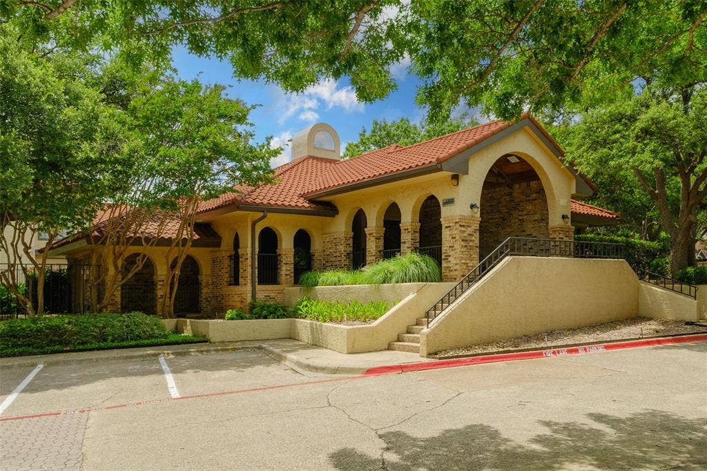 4130 Proton Drive, #47B, Addison, TX 75001 La Mirada's Spanish-style clubhouse featuring a clay tile roof, arched brick colonnade, and lush surrounding landscaping — available for residents and a testament to the community's well-maintained character.