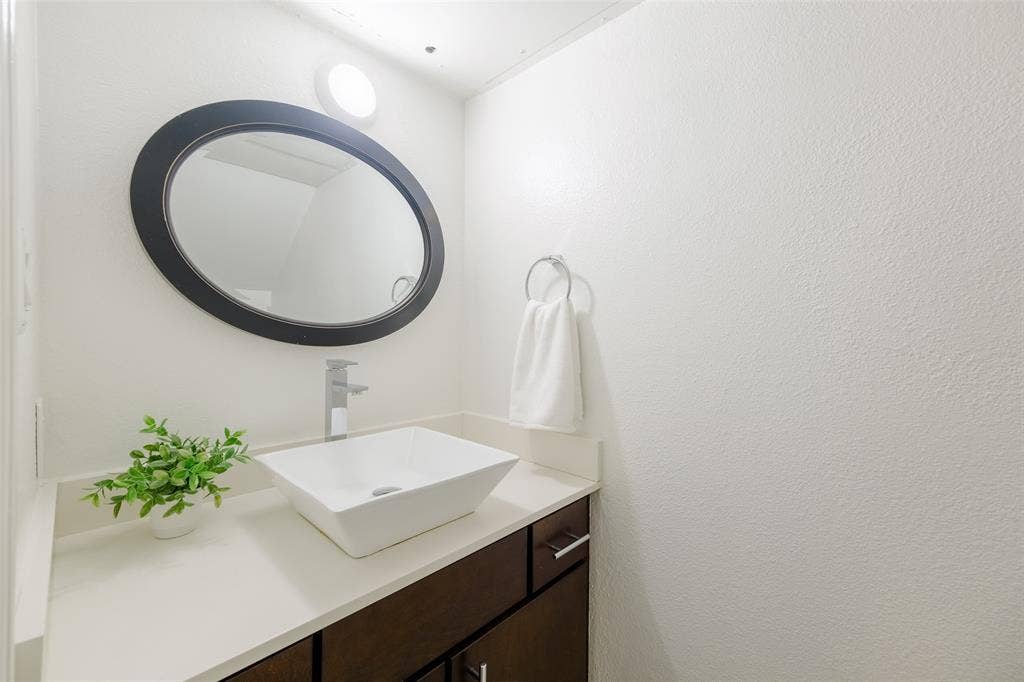 4130 Proton Drive, #47B, Addison, TX 75001 Updated half-bath with a white vessel sink, sleek chrome faucet, quartz countertop, and dark wood cabinetry — a modern, clean finish for guests.