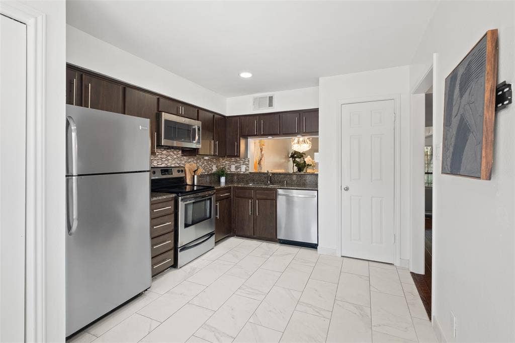 4130 Proton Drive, #47B, Addison, TX 75001 Well-appointed kitchen with full stainless steel appliance package including refrigerator, range, microwave, and dishwasher, complemented by dark cabinetry, granite counters, and a pass-through window to the dining room.