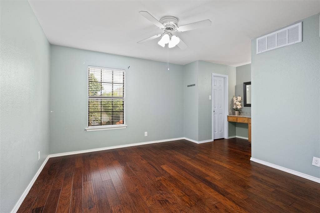4130 Proton Drive, #47B, Addison, TX 75001 Well-proportioned secondary bedroom with hardwood floors, a ceiling fan, natural light, closet, and a built-in vanity area with granite countertop — a versatile space for guest or office use.