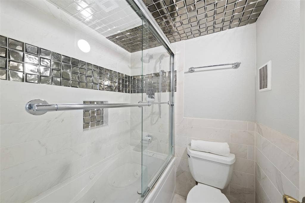 4130 Proton Drive, #47B, Addison, TX 75001 Secondary full bath with a tub/shower combo, glass slider door, reflective mosaic tile accents on the walls and ceiling, grab bar, and a recessed niche — a striking, one-of-a-kind finish.