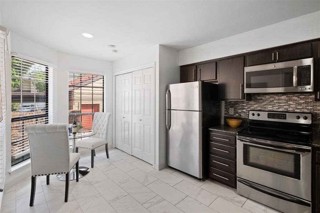 4130 Proton Drive, #47B, Addison, TX 75001 Updated kitchen featuring stainless steel appliances, dark espresso cabinetry, granite countertops, a mosaic tile backsplash, and a sunny breakfast nook with a bistro table and tree views.