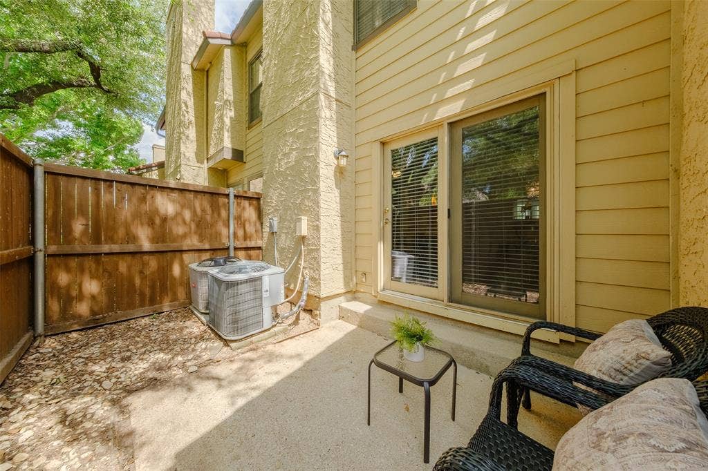 4130 Proton Drive, #47B, Addison, TX 75001 Rear patio with sliding glass door access, fenced privacy, wicker seating area, and established trees providing shade.