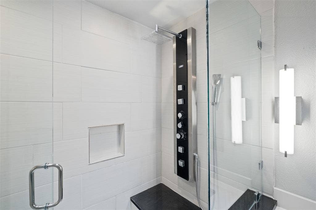 4130 Proton Drive, #47B, Addison, TX 75001 Walk-in shower with a full multi-function shower panel system, rainfall head, built-in niche, marble-look floor tile, and frameless glass enclosure with bench seating.
