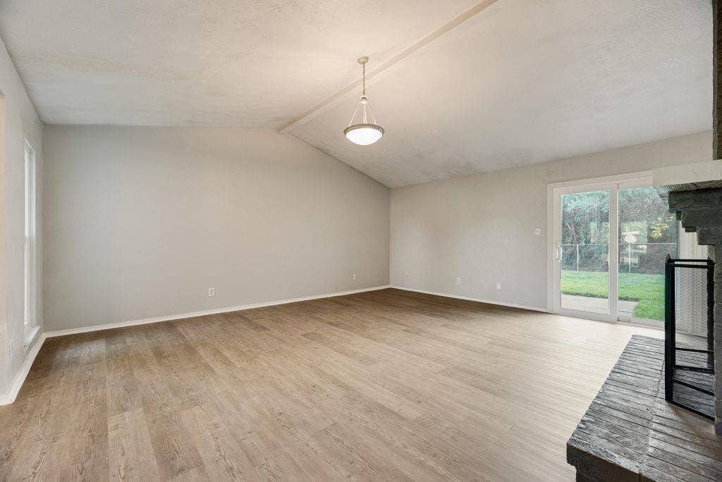316 Matterhorn Street, Cedar Hill, TX 75104 Spacious living area featuring vaulted ceilings, wood-finish flooring, and a stone fireplace with a black metal screen