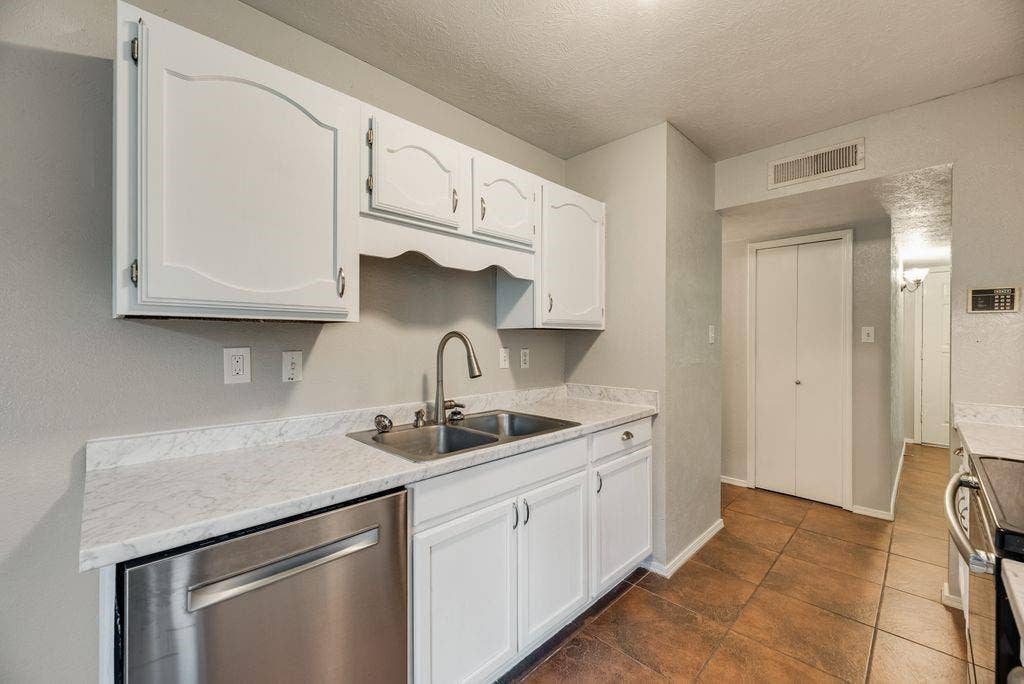 316 Matterhorn Street, Cedar Hill, TX 75104 Kitchen featuring white cabinetry, light-toned countertops, a stainless steel dishwasher, a double basin sink with a gooseneck faucet, and brown tile flooring