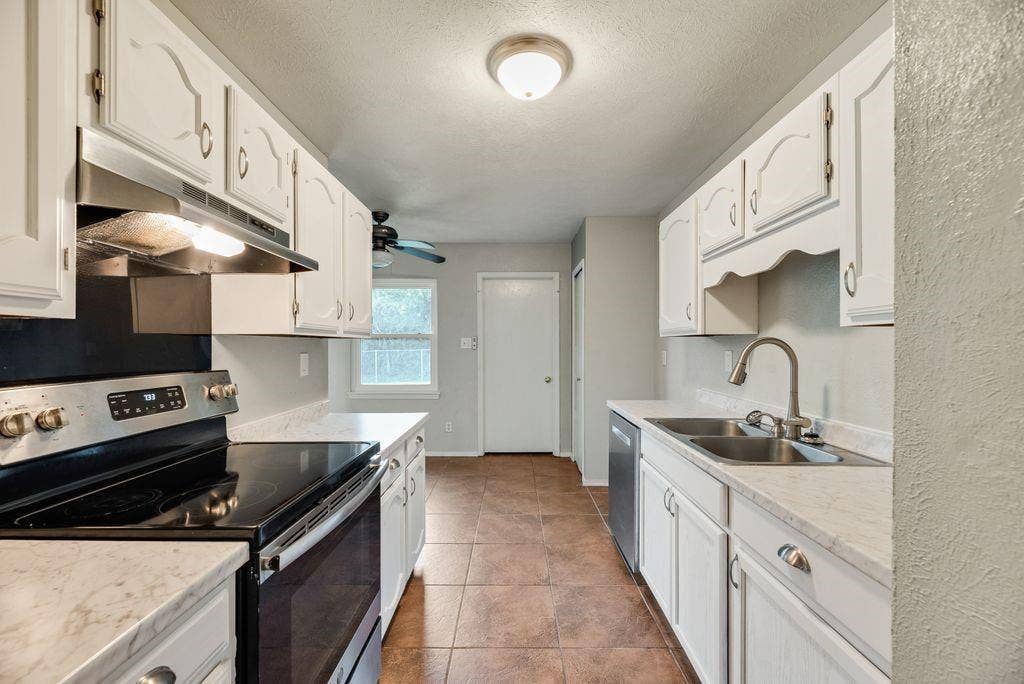 316 Matterhorn Street, Cedar Hill, TX 75104 Galley kitchen featuring white cabinetry, light countertops, tile flooring, and stainless steel appliances including a range and double basin sink