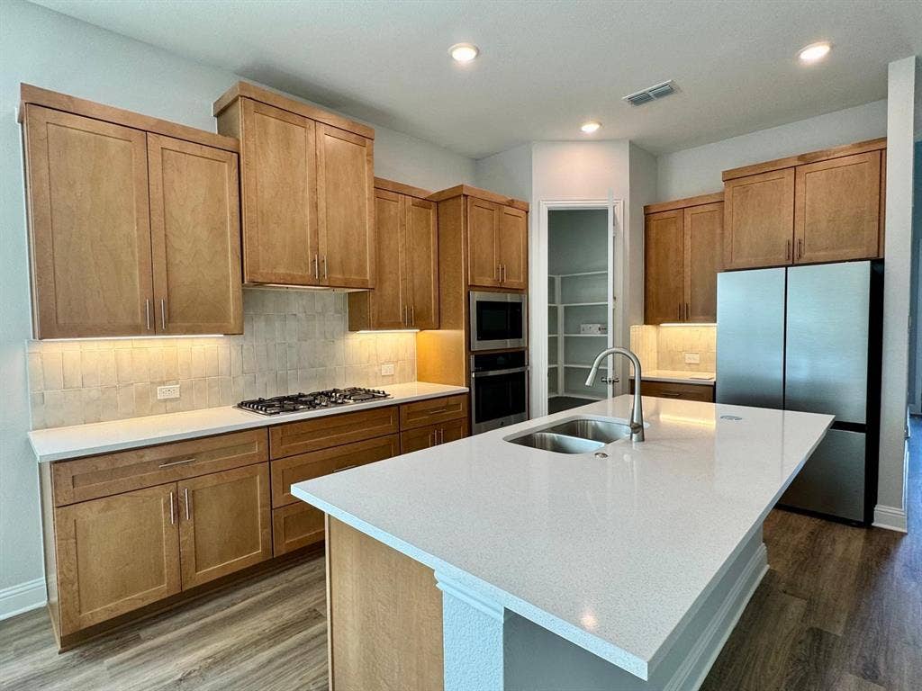 2930 Eleanor Drive, Prosper, TX 75078 Kitchen with appliances with stainless steel finishes, dark wood-style floors, light countertops, a kitchen island with sink, and recessed lighting