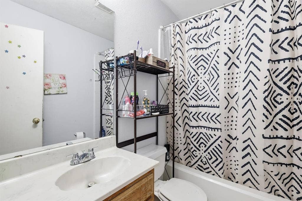 6406 Nicole Way, Arlington, TX 76002 Bathroom featuring a white vanity with integrated sink, chrome faucet, wood-finish vanity base, full-width mirror, and a white bathtub with a white toilet
