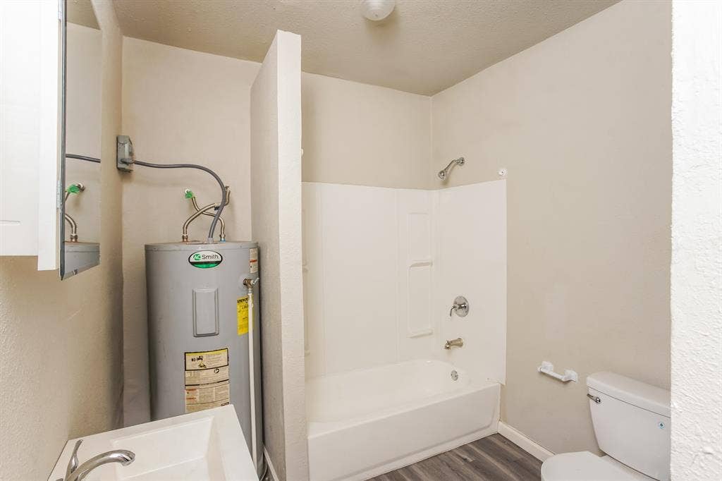 2402 Summer Avenue, Waco, TX 76708 Bathroom featuring a white shower-over-tub combination, a toilet, a sink with a chrome faucet, and wood-finish flooring