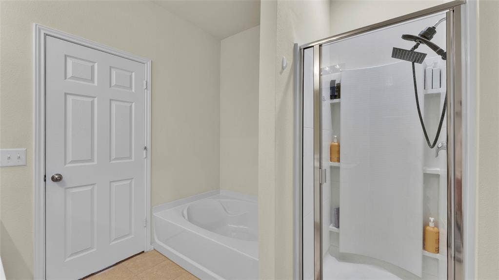 707 Indigo Road, Princeton, TX 75407 Bathroom featuring a soaking tub, a multi-function shower with a glass enclosure, built-in shower shelving, and a six-panel interior door