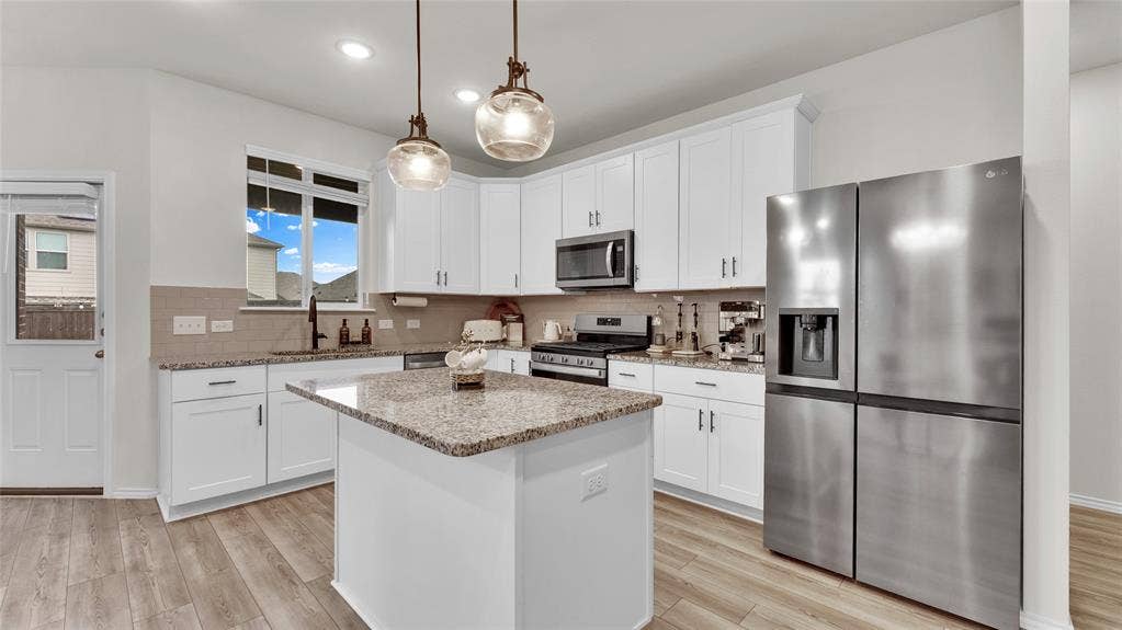 707 Indigo Road, Princeton, TX 75407 Modern kitchen featuring an island with granite countertops, white cabinetry, stainless steel appliances, wood-finish flooring, and pendant lighting