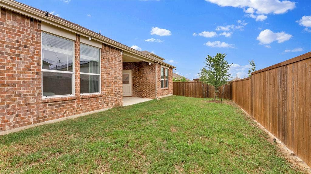 707 Indigo Road, Princeton, TX 75407 Private backyard featuring a covered patio, red brick exterior, wood privacy fencing, and a small tree