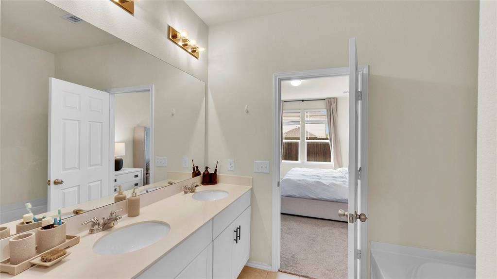 707 Indigo Road, Princeton, TX 75407 Bathroom featuring a dual vanity with undermount sinks, a large mirror, and a three-light fixture