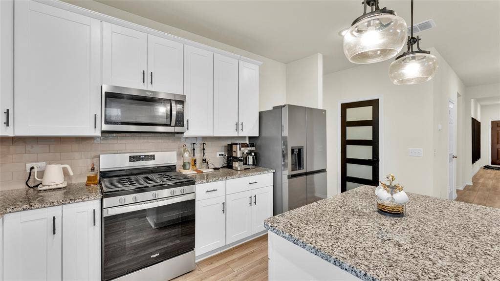 707 Indigo Road, Princeton, TX 75407 Modern kitchen featuring white shaker cabinetry, stainless steel appliances, speckled stone countertops, and a subway tile backsplash